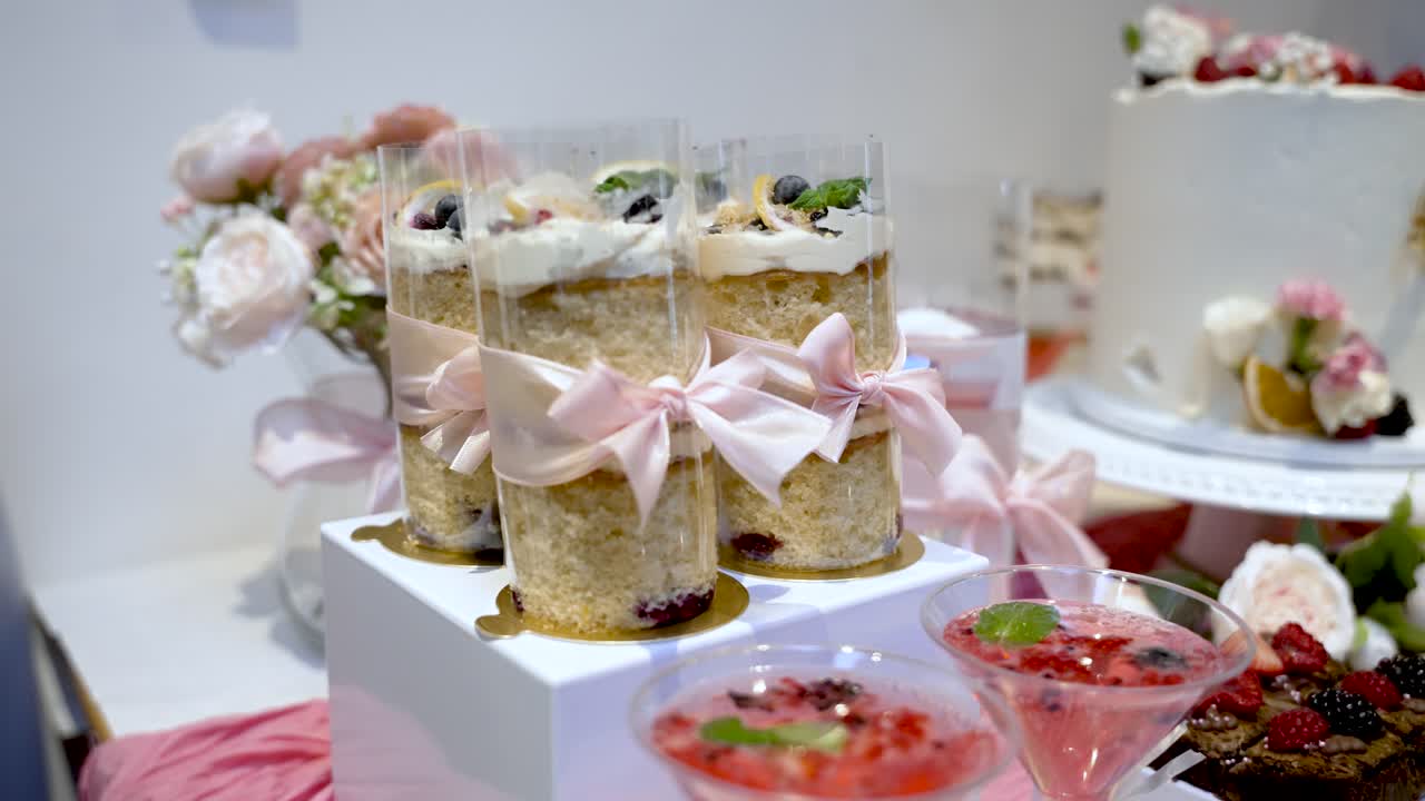 Elegant dessertbord med individuelle kager i klare kopper bundet med pink bånd sammen med cocktails med bær til fest og arrangementer