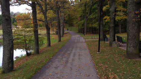 Park-pathway-in-dusk-time-in-autumn-season,-aerial-dolly-backward-view