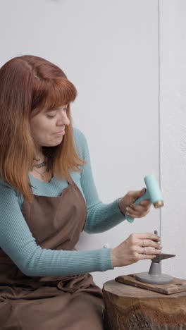 woman making jewelry with a hammer and anvil