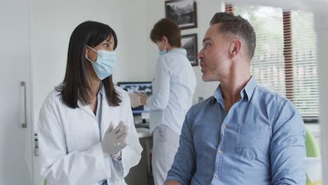 dentista biracial con máscara facial preparando a un paciente masculino en una clínica dental moderna