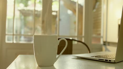 close-up of mug of coffee and laptop on dining table in kitchen of comfortable home 4k