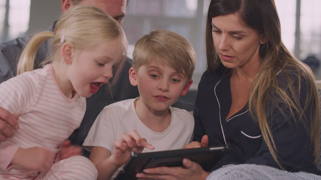 소파에 앉아 디지털 태블릿을 함께 사용하여 재미있는 피자마에 미소 짓는 가족