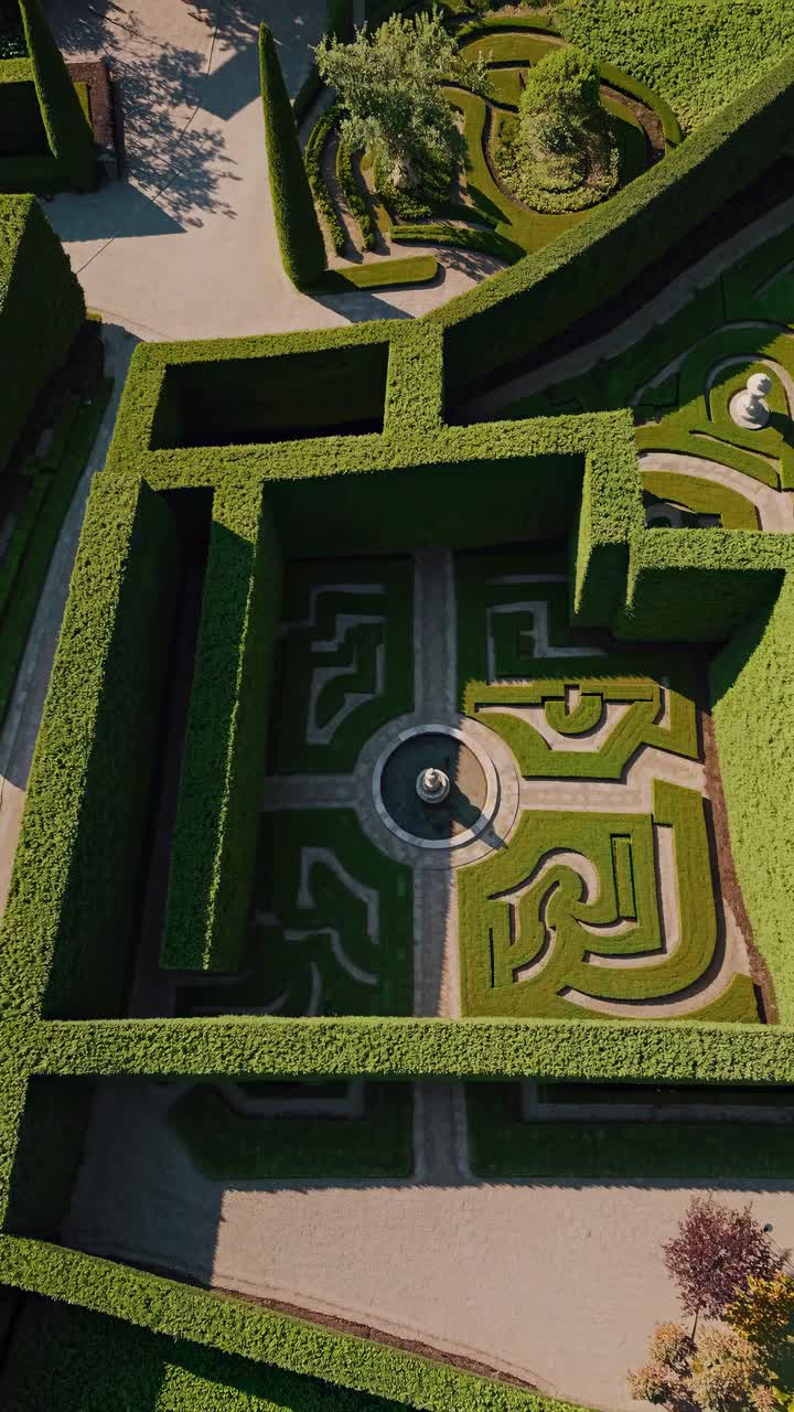 Aerial view of a geometric garden maze with hedges and a central fountain, resembling a video game