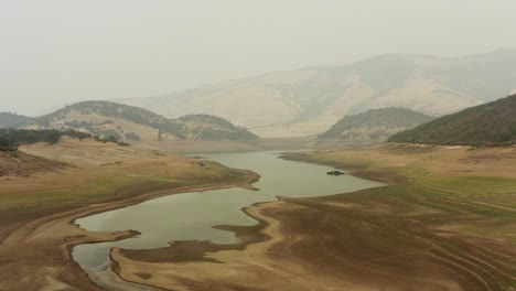 Slow-tracking-drone-shot-flying-over-a-mostly-dry-Emigrant-Lake-in-Southern-Oregon,-showing-smokey-drought-conditions
