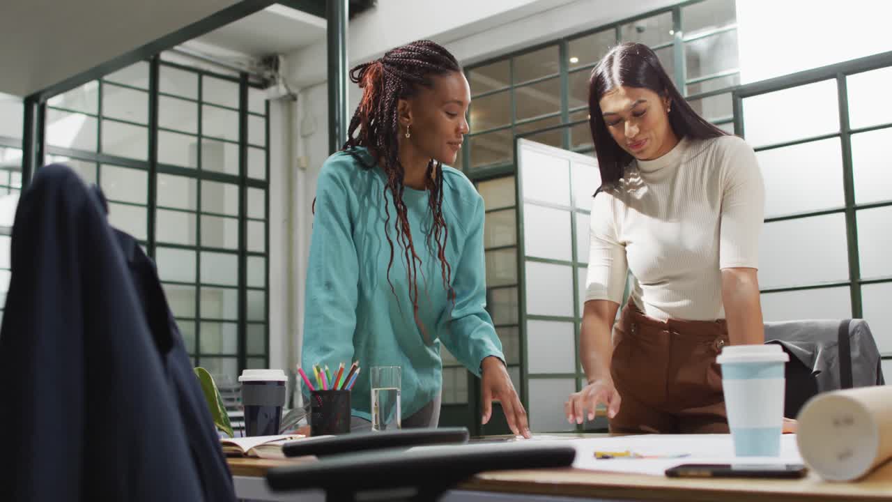 Happy diverse female architects looking at architectural blueprints and discussing work at office