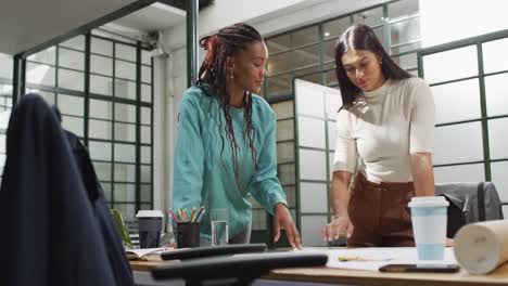 Happy-diverse-female-architects-looking-at-architectural-blueprints-and-discussing-work-at-office