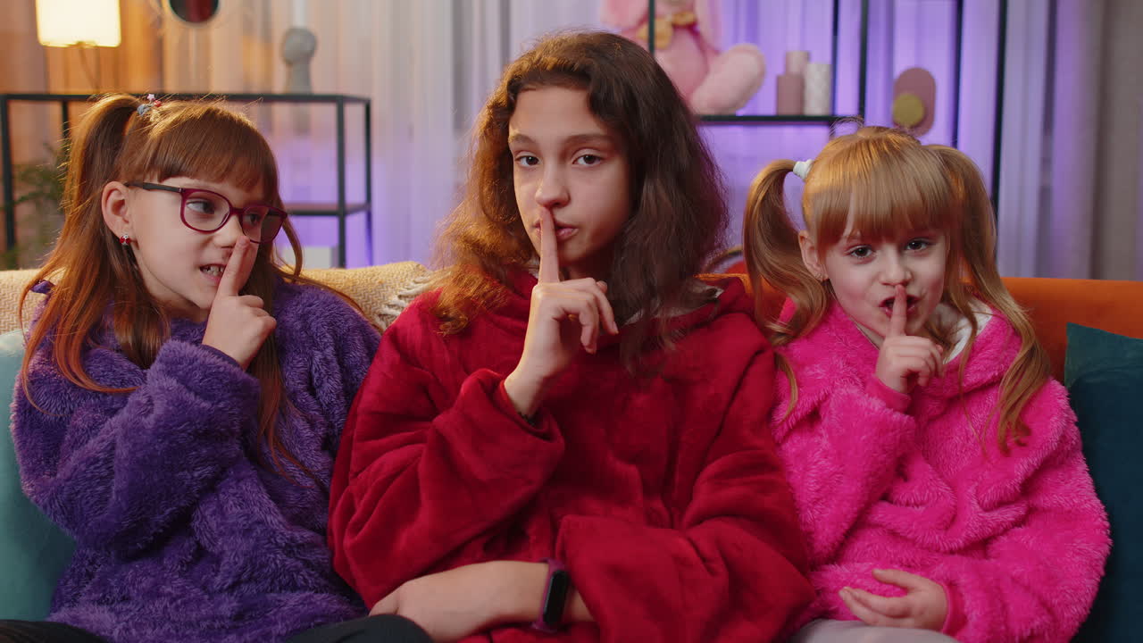 Siblings children girls presses index finger to lips makes silence gesture sign do not tell secret