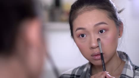 asian woman applying concealer under eyes