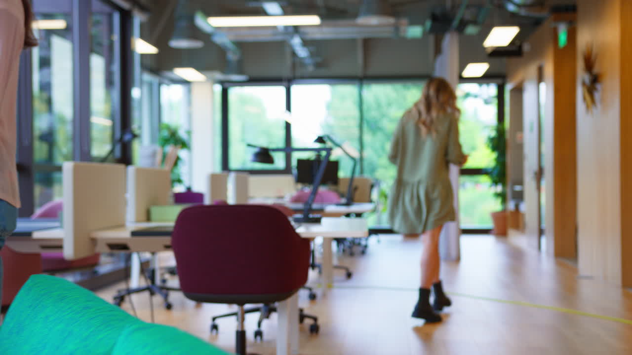 Businesswoman With Laptop Walking Through Office And Sitting In Breakout Seating Area To Work