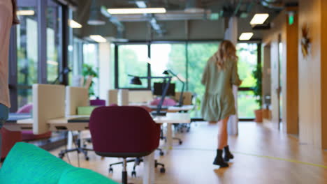 Businesswoman-With-Laptop-Walking-Through-Office-And-Sitting-In-Breakout-Seating-Area-To-Work