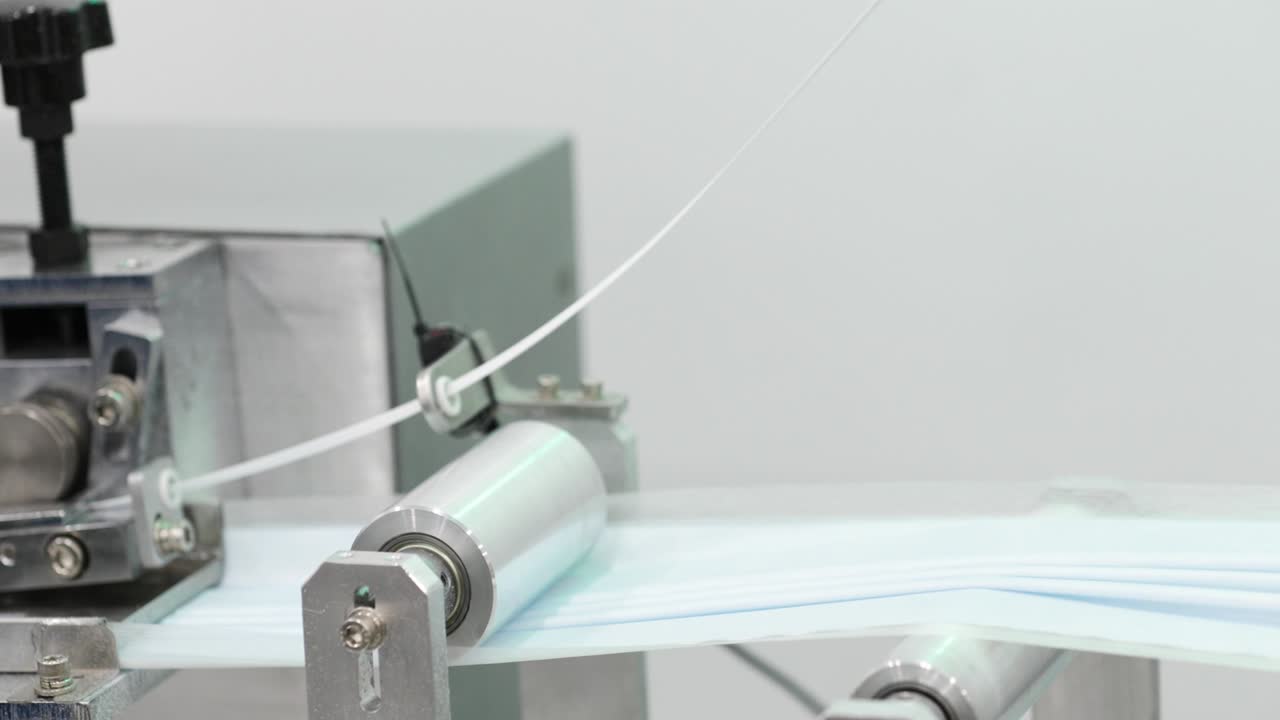 생산 라인 - 기계는 접힌 직물 스트립을 금속 롤러로 압축합니다.