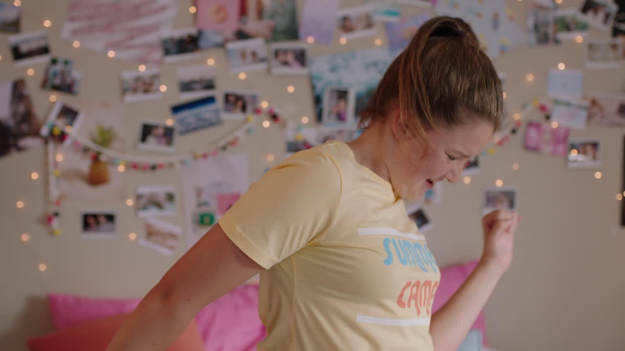 행복한 십대 소녀는 침실에서 춤을 추고 재미있는 춤을 추고 주말을 축하하고 긍정적인 느낌으로 집에서 잠옷을 입고 있습니다.