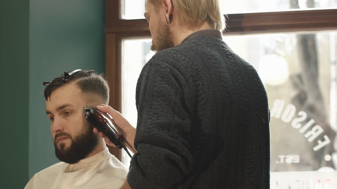 Barbiere che taglia i capelli a un uomo con il tagliacapelli in una barberia