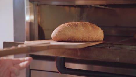 Freshly-baked-loaf-of-bread-being-taken-out-of-an-oven-in-slow-motion,-warm-kitchen-ambiance