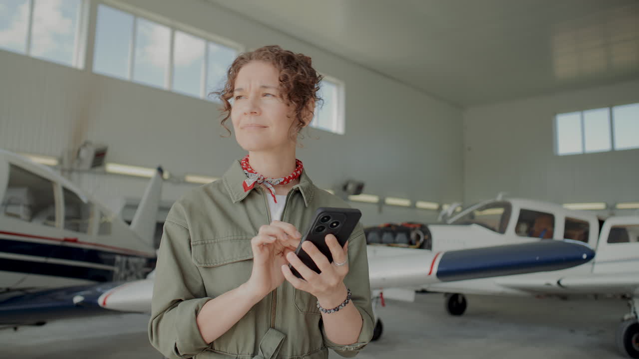 Female Tehnician Texting on Phone during Work Break in Aviation Hangar