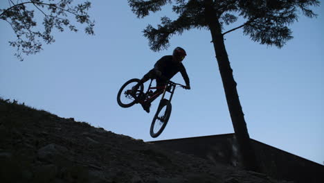 slow motion shot of downhill racer hitting a big jump with a whip, only silhouette is visible against blue sky. downhill park in semmering austria. footage slowed down eight times