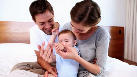 Happy-parents-sitting-on-bed-with-their-baby-son