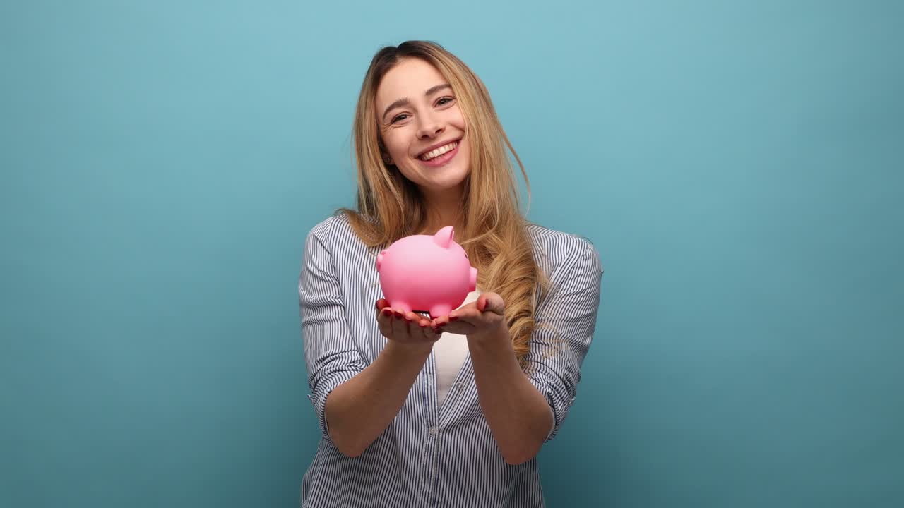 Smiling positive woman holding piggy bank, suggesting you to put coins inside, saving money.