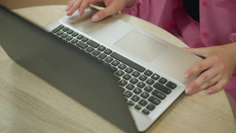 hand view of lady wearing pink dress and wrist chain opening laptop on a wooden table, with shadow visible on keyboard, preparing to type, as the laptop screen is opened, with the place well lit up