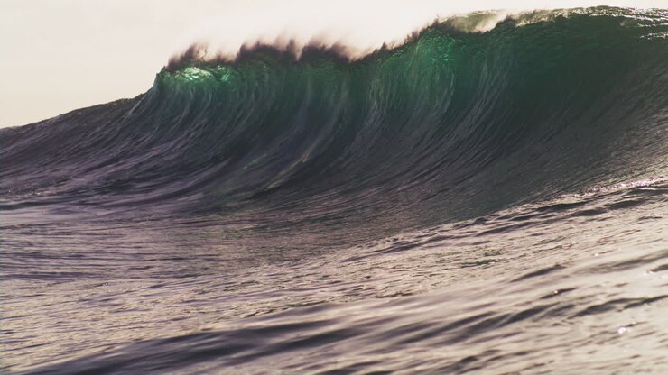 Sun flare of light glows gently as wave glows green with spray and mist