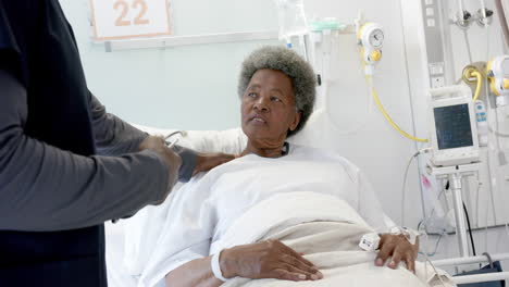 african american male doctor talking with female senior patient in hospital room, slow motion