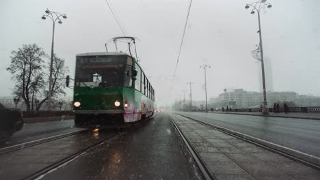 snowy and rainy city street scene with tram and cars