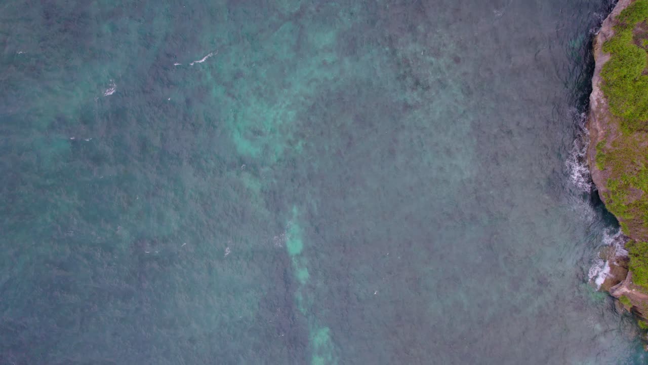 Spiaggia curva con acque blu poco profonde e promontori rigogliosi a Dream Beach Indonesia, sfondo ripreso con drone dall'alto