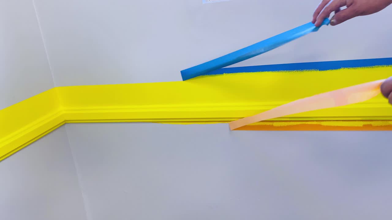 Painter removes masking tape from freshly painted wall with yellow stripe decor