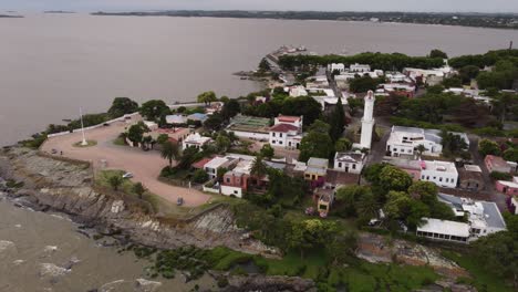 Toma-De-órbita-Aérea-Del-Faro-Y-La-Costa-De-La-Ciudad-De-Colonia-Del-Sacramento-En-Uruguay-Durante-El-Día-Nublado-Oscuro