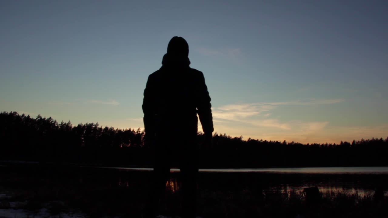Young silhouetted man wearing hat stops and looks at pretty sunset