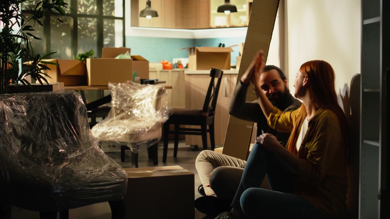Happy Couple Sitting on Floor in New Home Surrounded by Moving Boxes