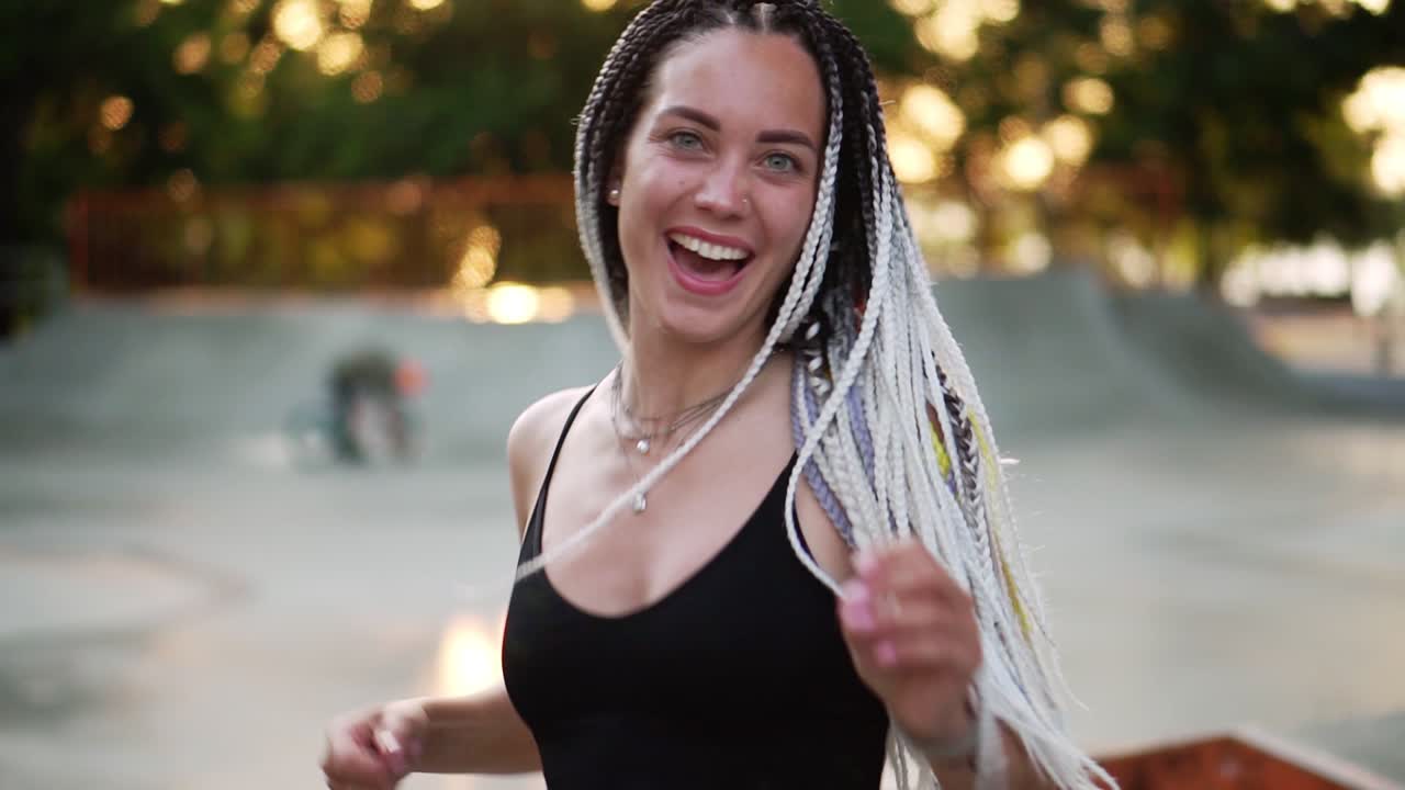 chica alegre con rastas bailando en un parque. hermosa mujer en negro arriba bailando activamente durante un día soleado. sonriendo a