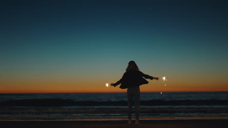 girl dancing with sparklers on beach at sunset celebrating new years eve woman having fun dance with sparkler fireworks enjoying independence day celebration by the sea