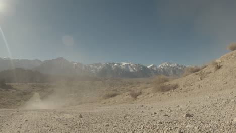 a vehicle drives over the camera along a dirt road towards mt. whitney and the eastern sierra nevada snow-capped mountains