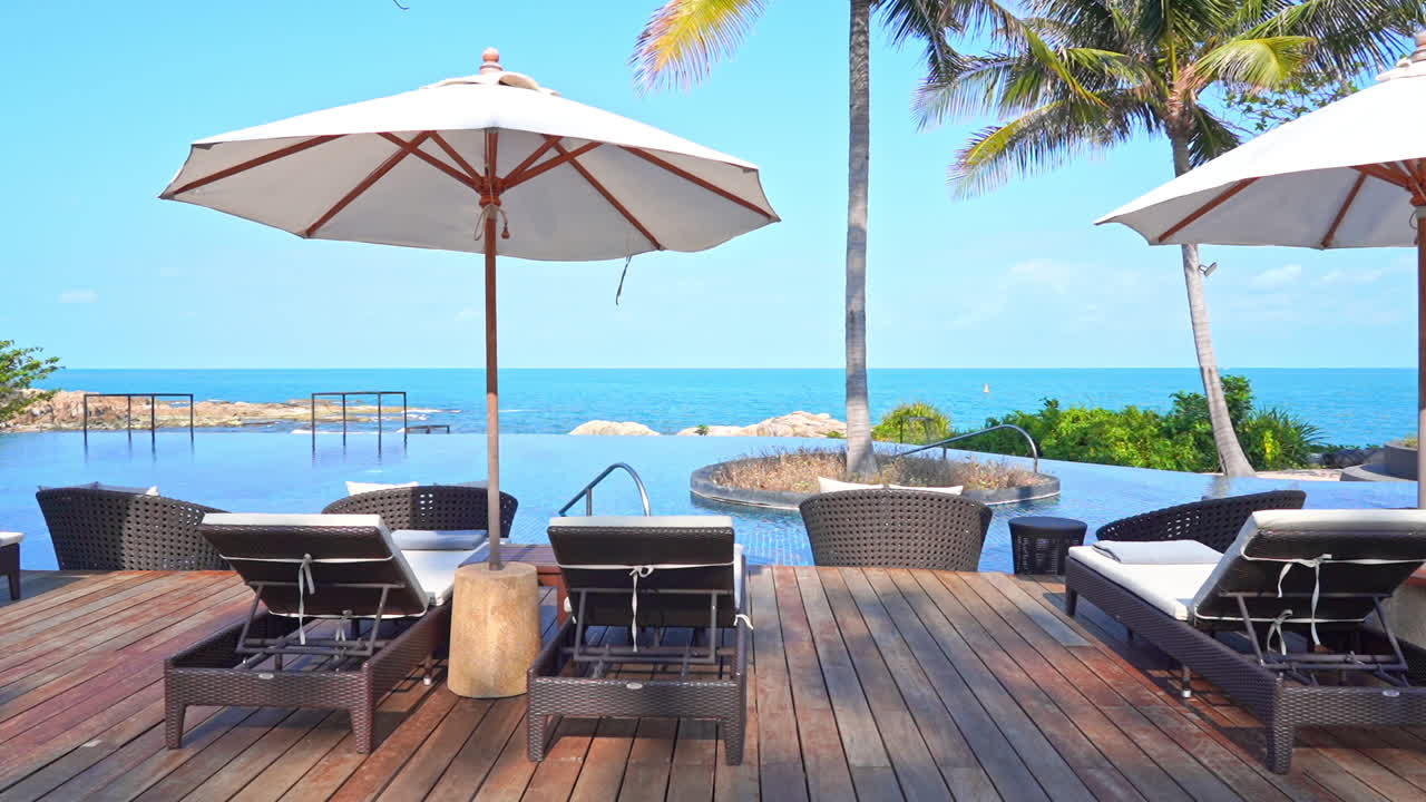 빈 라운지 의자와 비치 파라솔은 바다 전망을 감상할 수 있는 리조트 수영장을 둘러싼 데크에 있습니다.