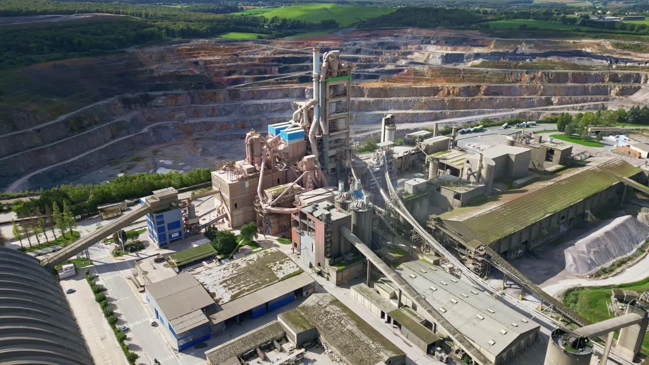 A drone orbiting shot captures the cement factory in Saint-Pierre-la-Cour, highlighting its industrial structures with the quarry visible in the background