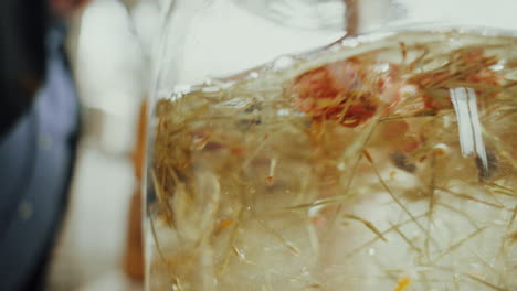 close up shot, mixing distilled gin inside a glass bottle with aromatic dried spice herbs