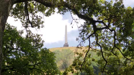 un obelisco en la cima de una colina de árboles visto a través de los árboles en la ciudad de auckland, nueva zelanda, con nubes en el cielo en un día soleado y azul