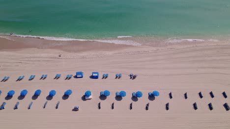 Stunning-view-of-beach-chairs-and-umbrellas-flying-over-the-sand-and-blue-beach-water-blue-sky-palm-trees-ft