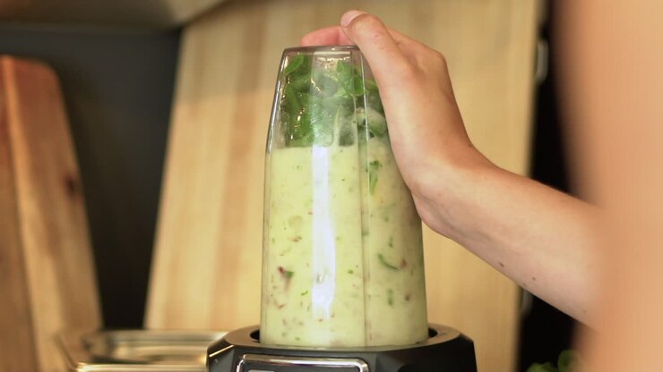 Nahaufnahme von weiblichen Händen, die mit einem Mixer einen Smoothie zubereiten