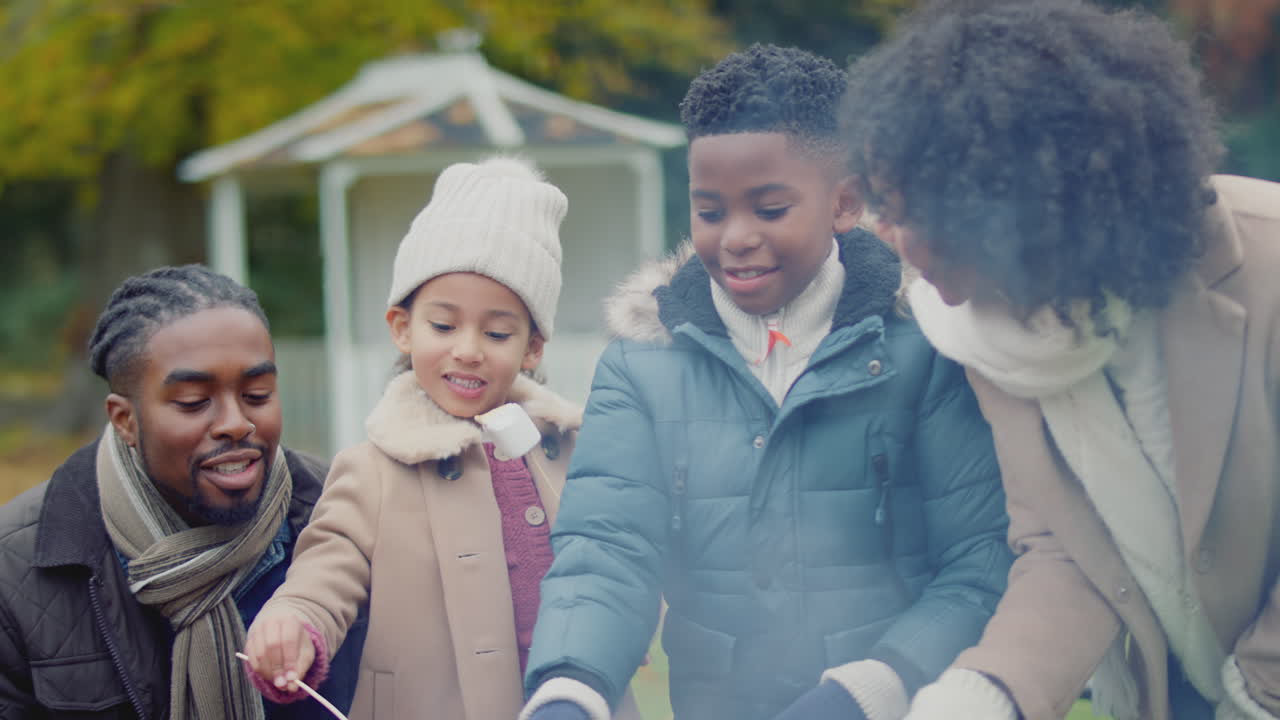 familia tostando y comiendo marshmallows sentados alrededor de la chimenea o barbacoa en el jardín en casa - disparado en cámara lenta