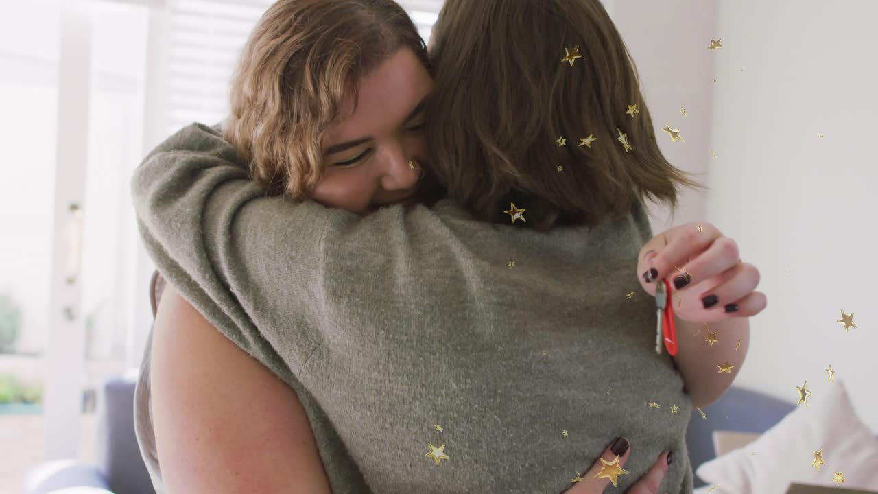 Two women hugging in home, producing red keychain house key celebrating real estate with confetti