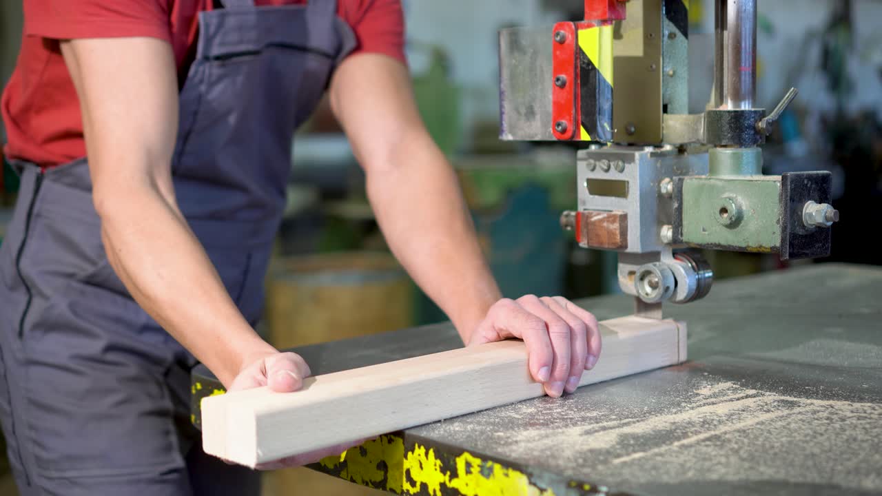 A man cutting a piece of wood with a band saw in a workshop