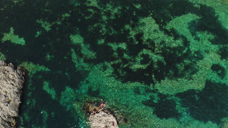 Aerial-Drone-Shot-of-a-Rock-surrounded-by-crystal-clear-water-in-Mallorca,-Spain,-4k