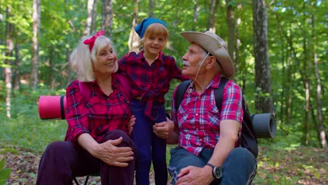 abuela abuelo y niño niño niña familia excursionistas turistas sentados en el bosque, abrazándose, besándose