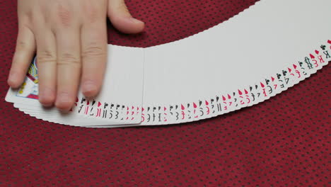primer plano de un jugador experto que extiende una baraja de cartas en una mesa de juego roja