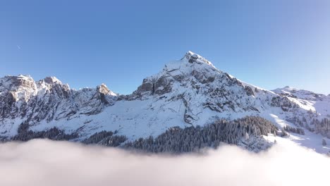 fronalpstock mountain in glarus, switzerland, with snow covered peaks above serene cloud layers, drone view of winter alpine landscape.