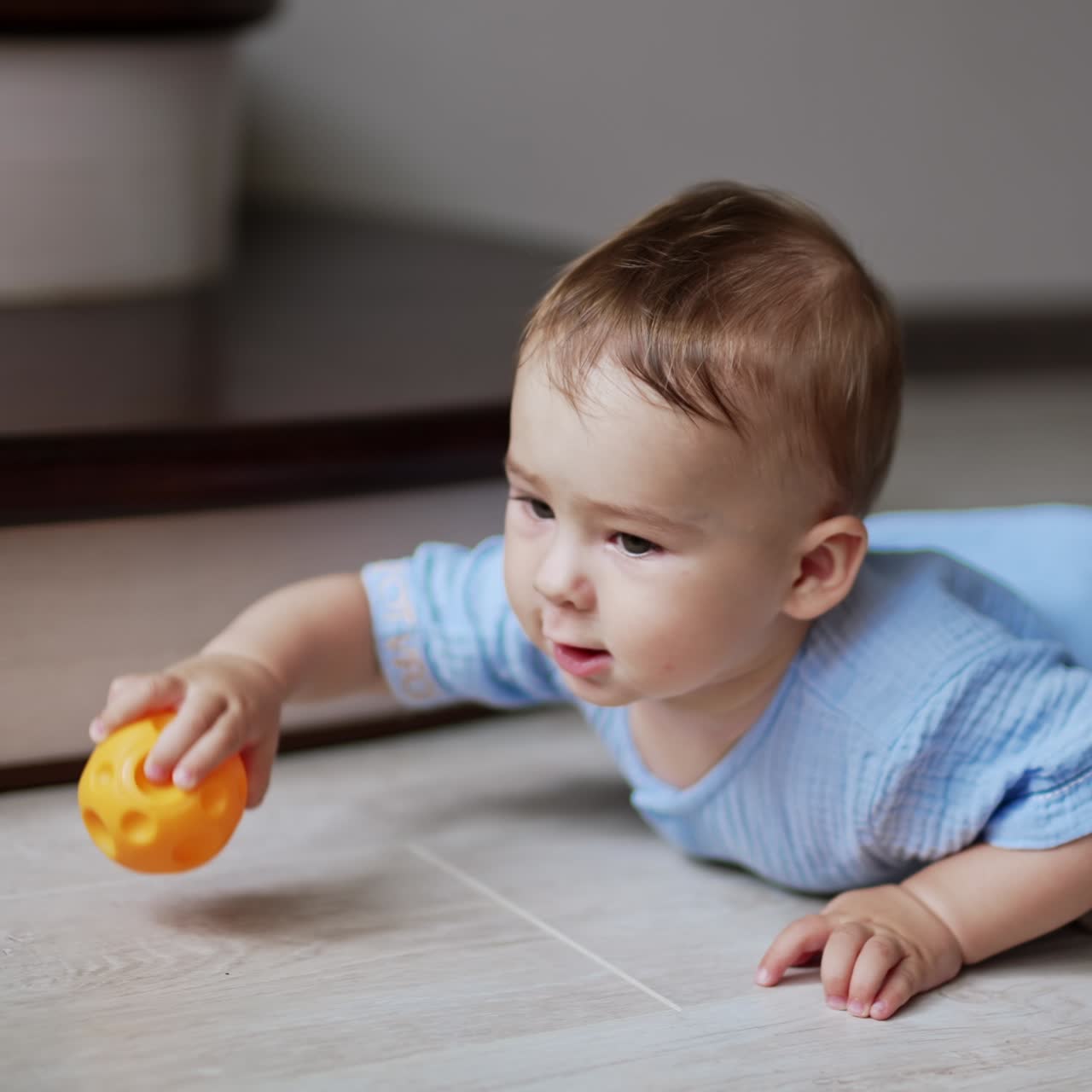 Sweet adorable baby boy crawling by the floor indoors. Active healthy kid trying to reach a ball. Little kid playing with a toy