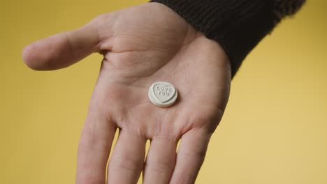 Close-Up-Of-Hand-Holding-Heart-Candy-With-Love-You-Message-On-Yellow-Background-1