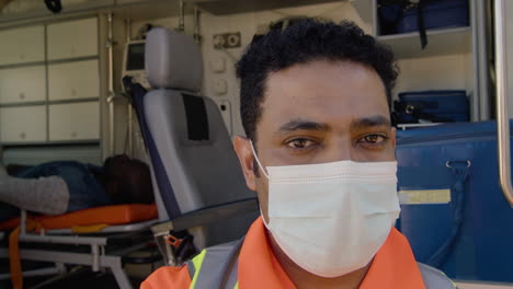 portrait of a latin male paramedic with face mask standing in front of an ambulance and looking at the camera